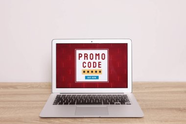 Beyaz duvarın yanındaki tahta masada aktif promosyon kodlu dizüstü bilgisayar.