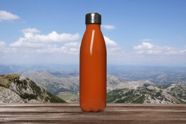 Ahşap masada turuncu termik şişe ve güzel dağ manzarası.
