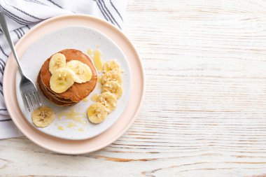 Plate of banana pancakes with honey served on white wooden table, top view. Space for text