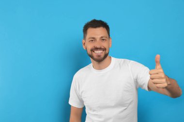 Açık mavi arkaplanda baş parmağını gösteren adam, metin için boşluk