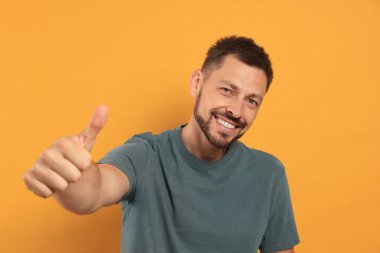 Adam turuncu arka planda baş parmağını gösteriyor.