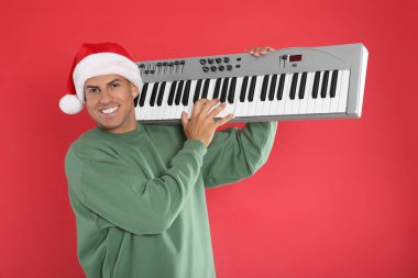 Kırmızı arka planda sentezleyici çalan Noel Baba şapkalı adam. Noel müziği