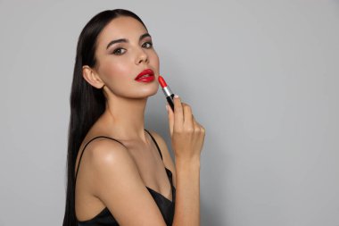 Güzel makyajlı genç bir kadın açık gri arka planda kırmızı ruj tutuyor, mesaj için yer var.