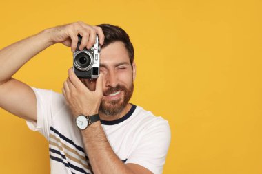 Kameralı adam sarı arkaplanda fotoğraf çekiyor, mesaj için yer var. İlginç bir hobi.