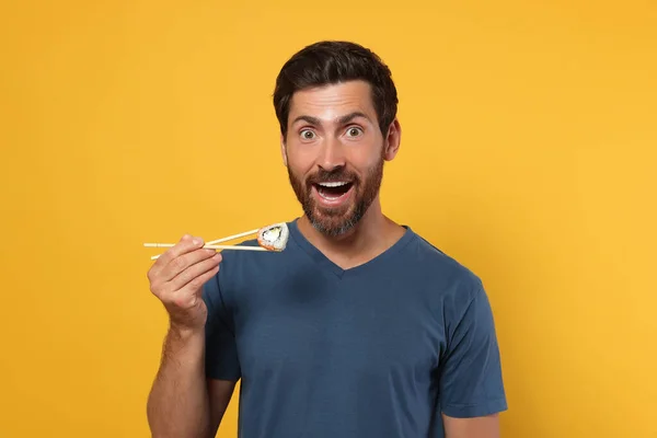 Emocionální Muž Drží Sushi Roll Hůlkami Oranžovém Pozadí — Stock fotografie