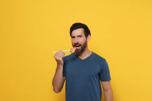 オレンジを背景に箸で寿司を食べるハンサムな男 — ストック写真