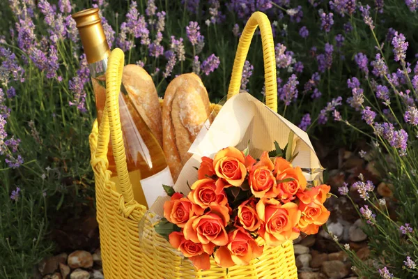 户外薰衣草花边的黄色柳条袋 上面有美丽的玫瑰 酒瓶和面包 — 图库照片