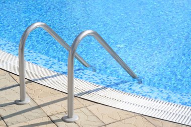 Outdoor swimming pool with ladder and handrails on sunny day
