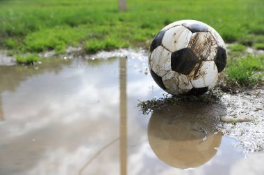 Açık hava birikintisinin yakınındaki yeşil çimlerde kirli futbol topu, metin için yer