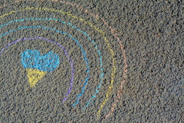 Rainbow with heart drawn by blue and yellow chalk on asphalt, top view