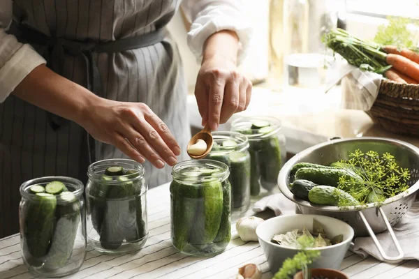 Woman putting garlic into jar in kitchen, closeup. Canning vegetables