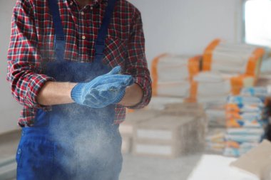 Construction worker shaking off dust from hands in room prepared for renovation, closeup