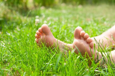 Child sitting barefoot on green grass outdoors, closeup clipart