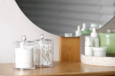 Containers with cotton swabs and pads near cosmetic products on dressing table