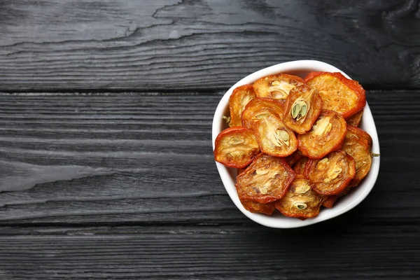 Bowl with cut dried kumquat fruits on black wooden table, top view. Space for text