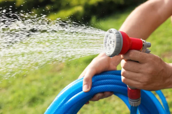 Man spraying water from hose in garden, closeup