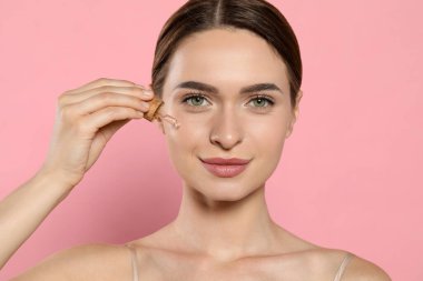 Pembe arka planda yüzüne gerekli yağı süren genç bir kadın.