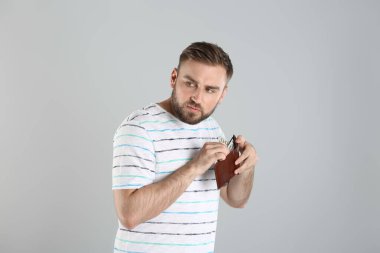 Açgözlü genç adam, açık gri arka planda parası olan bir cüzdan saklıyor.