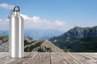 Tahta masadaki alüminyum su şişesi ve güzel dağ manzarası, yazı için yer.