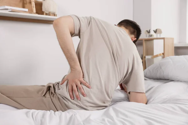 部屋のベッドに座りながら腰痛に苦しむ男 大腸炎の症状 — ストック写真