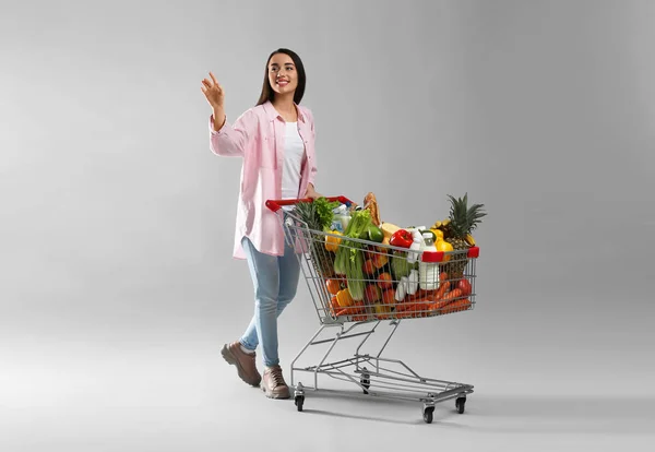 Junge Frau Mit Einkaufswagen Voller Lebensmittel Auf Grauem Hintergrund — Stockfoto