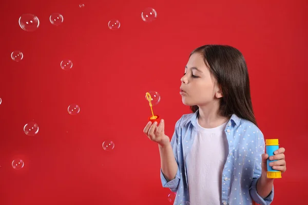 Маленькая Девочка Надувает Мыльные Пузыри Красном Фоне — стоковое фото