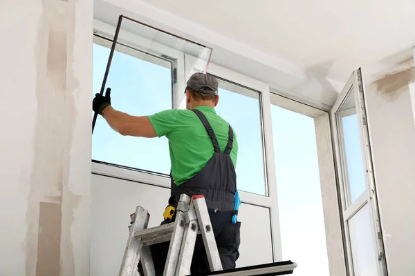 Worker on folding ladder installing window indoors