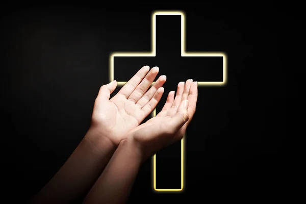 Christian cross and woman stretching hands towards light in darkness, closeup