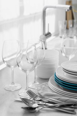 Mutfaktaki tezgahta farklı temiz bulaşık takımı, çatal bıçak ve bardaklar var.