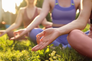 Dışarıdaki yeşil çimlerde meditasyon yapan kadınlar, yakın plan. Sabah yogası