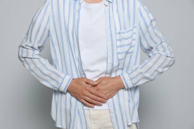 Açık gri arka planda adet sancısı çeken genç bir kadın, yakın plan.