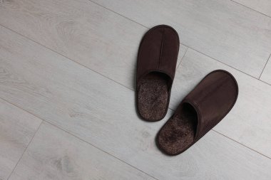 Pair of brown slippers on wooden floor, top view. Space for text