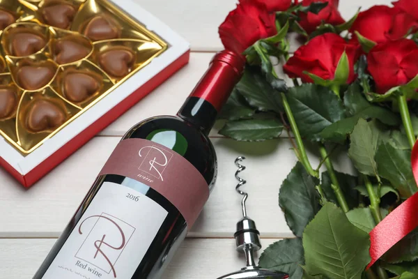 红葡萄酒瓶 美丽的玫瑰和心形巧克力糖果放在白色木制桌子上 — 图库照片