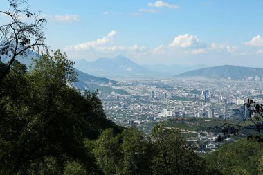 Şehirdeki güzel gökyüzünün altında ağaçların, binaların ve dağların manzarası.