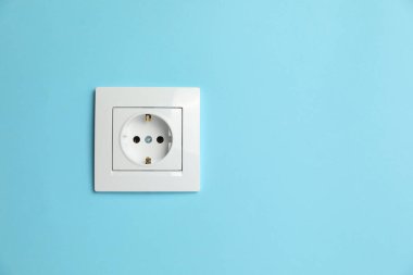 Power socket on light blue wall, space for text. Electrical supply
