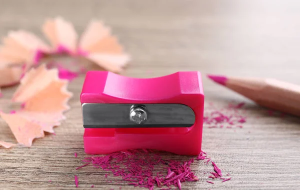 Pink sharpener, pencil and shavings on wooden table, closeup