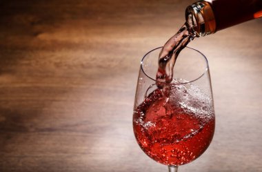 Şişe şişesinden cam camına gül şarabı dökerek, ahşap masaya, yakın plan. Metin için boşluk