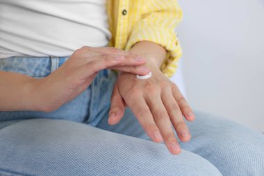 Woman applying cream on her hand against white background, closeup