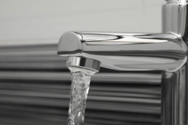 Water flowing from tap on blurred background, closeup