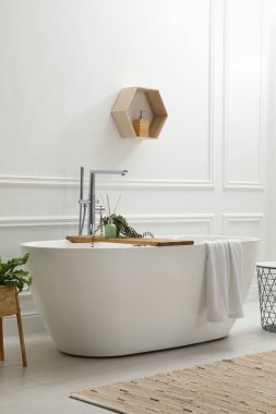 Modern seramik küvet ve beyaz duvarın yanında yeşil bitkiler.