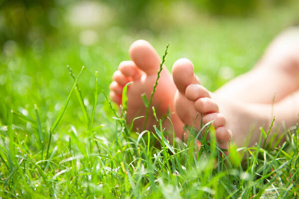 Ребенок сидит босиком на зеленой траве на открытом воздухе, крупным планом