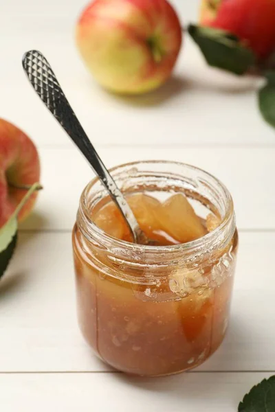 Tasty apple jam in glass jar and fresh fruit on white wooden table