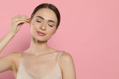 Pembe arkaplan üzerine gerekli yağı uygulayan genç bir kadın, metin için boşluk
