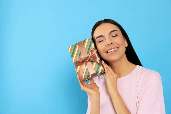 快乐的年轻女人拿着浅蓝色背景的礼品盒 — 图库照片