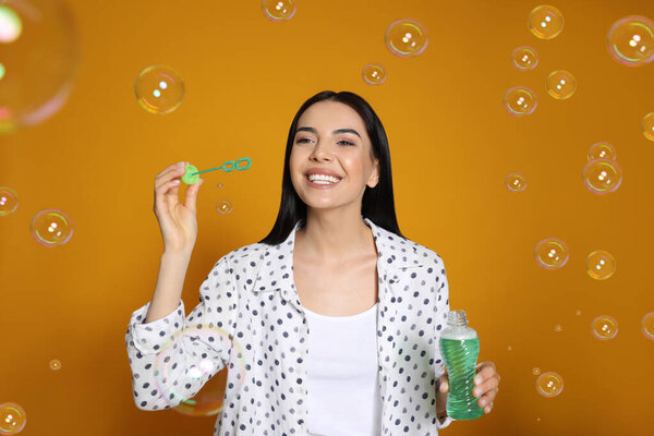 Young woman blowing soap bubbles on yellow background