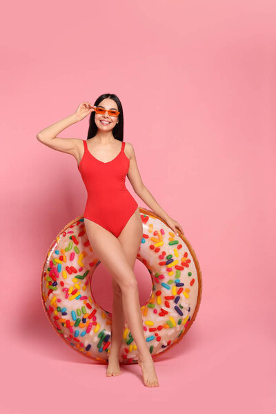 Young woman with stylish sunglasses holding inflatable ring against pink background