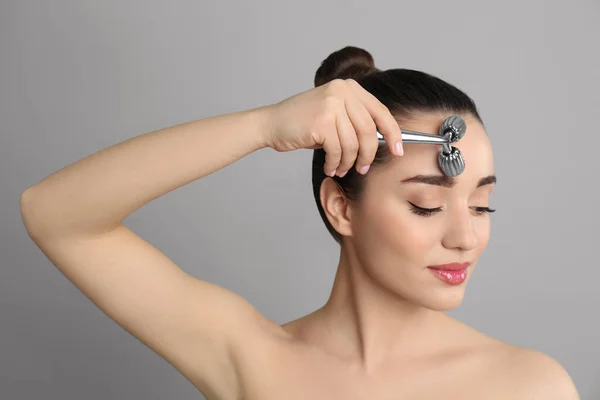 Woman using metal face roller on grey background