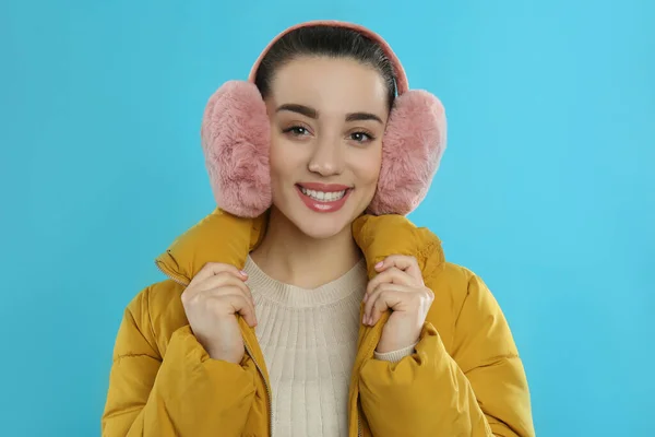 美しいです若いです女性身に着けていますEarmuff上のライトブルーの背景 — ストック写真