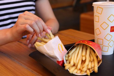 MYKOLAIV, UKRAINE - 11 Ağustos 2021: McDonald 's patates kızartmalı ve kafedeki masada içen kadın, yakın plan
