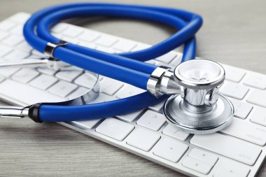 Computer keyboard with stethoscope on wooden table, closeup